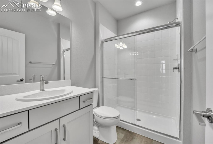 Full bath featuring a shower stall, wood finished floors, vanity, toilet, and recessed lighting